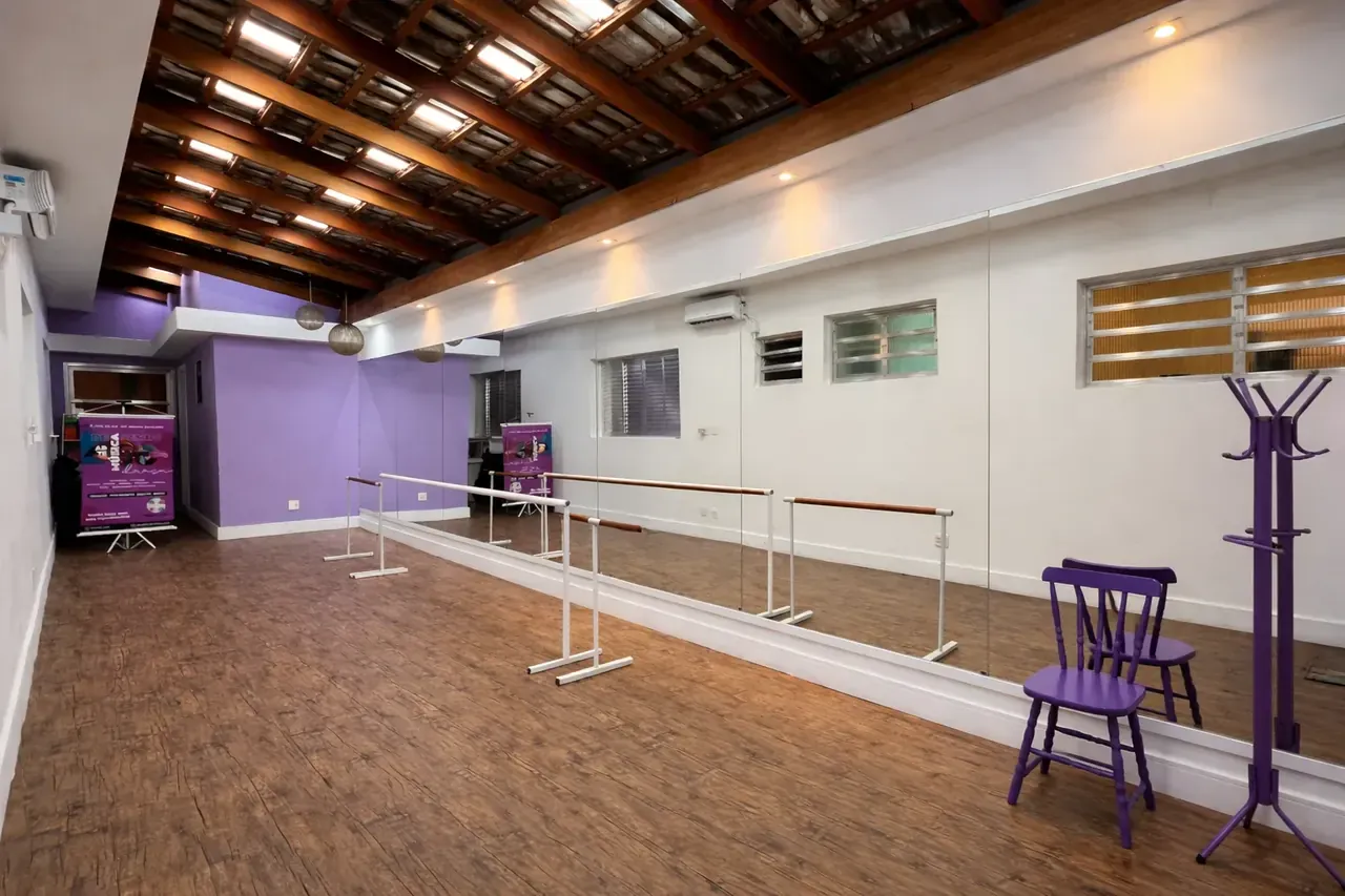 Sala de dança com piso de madeira, parede lilás, espelhos e barras de ballet