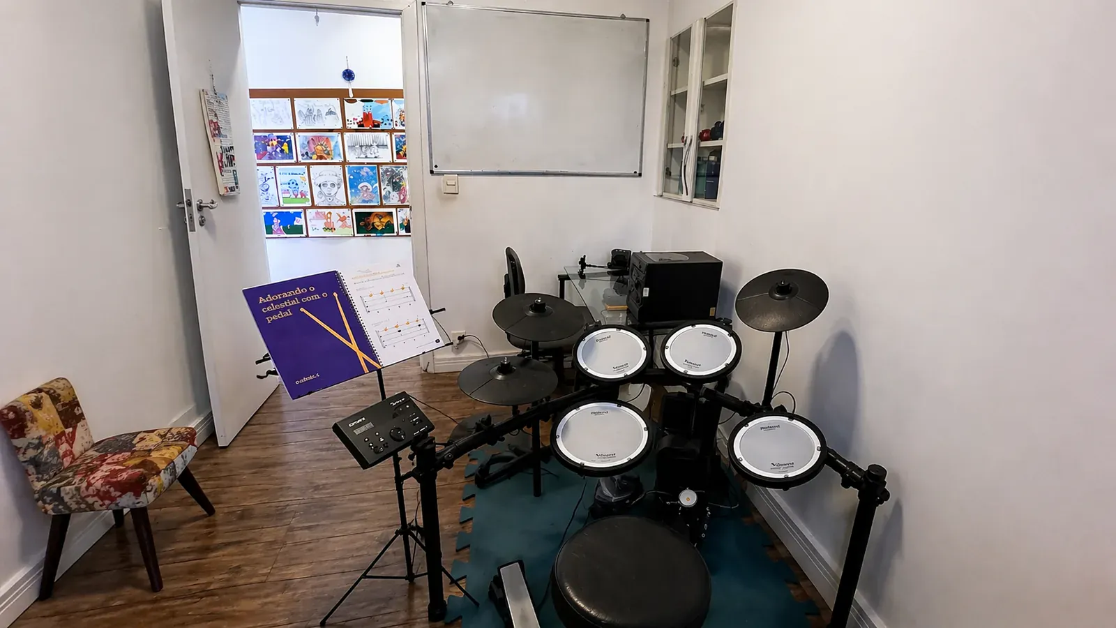Sala de bateria com bateria eletrônica Roland, estante de partituras e cadeira estampada