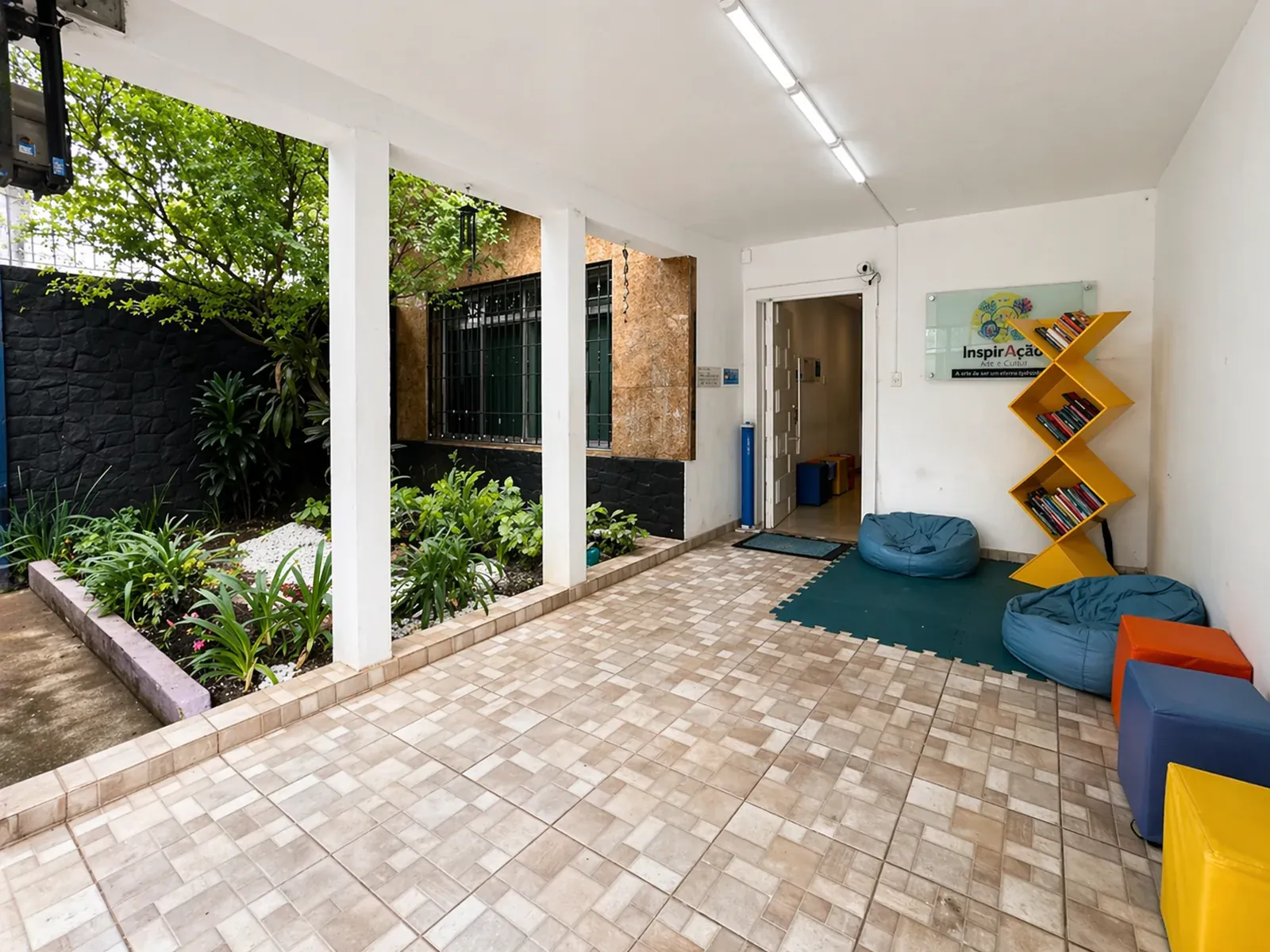 Entrada do Centro Cultural InspirAção com jardim, pufes e estante de livros